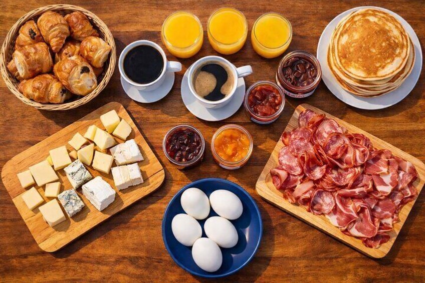 Una mesa de desayuno con pasteles, queso, huevos, jamón y bebidas. 2