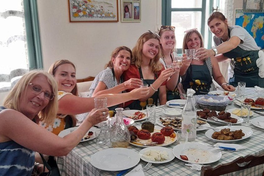 Un groupe de personnes est assis autour d’une table, devant de la nourriture et des boissons, et porte un toast en levant leurs verres. 1