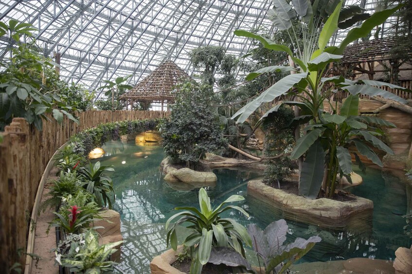 An indoor botanical garden with a glass ceiling, a central water feature, and various tropical plants. 2