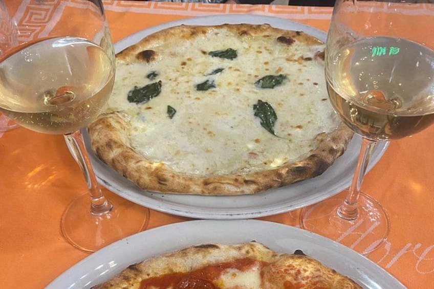 Deux pizzas servies sur des assiettes, accompagnées chacune d’un verre de vin blanc. 1