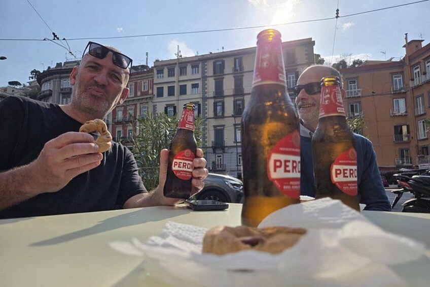 Deux personnes sont assises à une table devant des bouteilles de bière PERDO et une assiette remplie de nourriture. 5