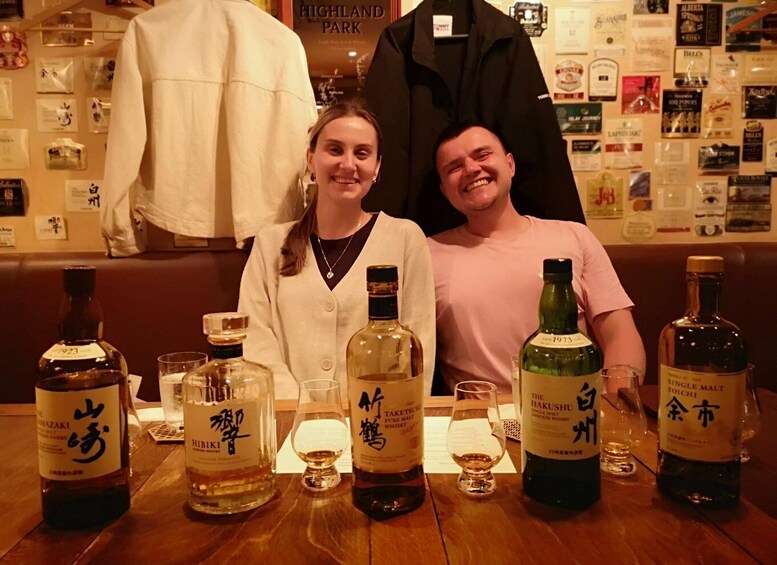 Une personne assise à une table devant laquelle se trouvent différentes bouteilles de spiritueux et des verres. 1