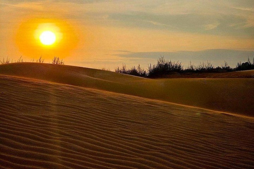A desert landscape with rolling sand dunes and a setting sun. 2