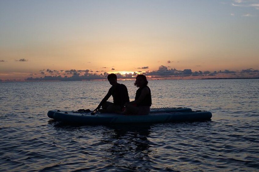 Dos personas sentadas en una balsa sobre aguas tranquilas durante el atardecer. 3