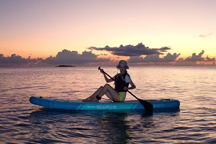 Una persona sentada en un kayak azul sobre aguas tranquilas durante la puesta de sol. 1