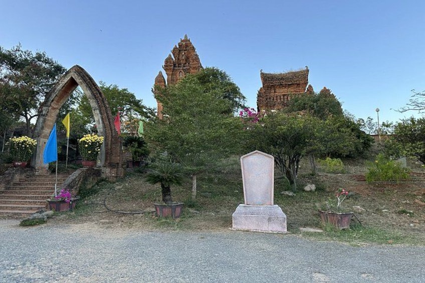 A temple with a stone archway, a stone monument, and a large pagoda in the background. 1