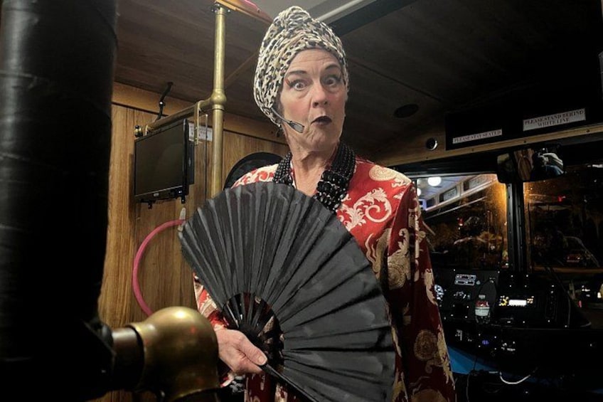 A person in a red patterned outfit holding a black fan, standing in a room with wooden walls and various equipment. 2