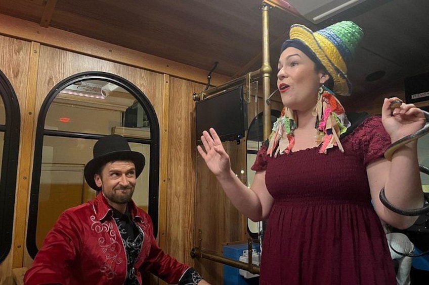 A person in a red jacket and hat, another in a maroon dress with a colorful hat, and a wooden interior with a circular window. 3