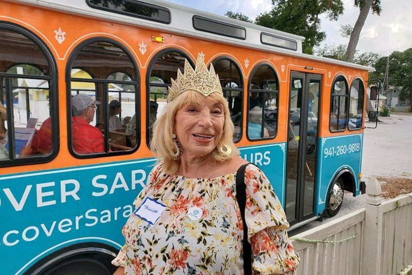 A woman in a floral dress and crown standing in front of a bus with 'COVER SAR' and a phone number on it. 4