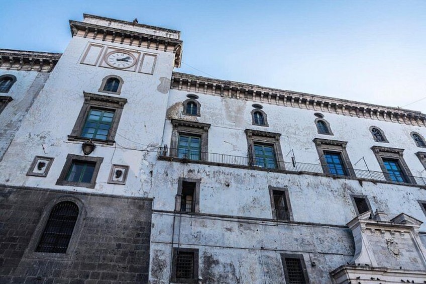 A historic building with a clock tower, arched windows, and a weathered facade. 2