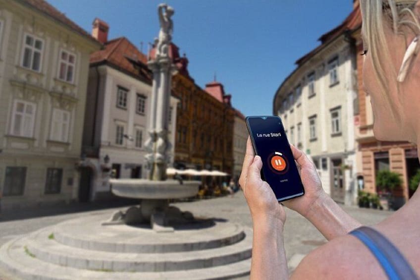 En person som håller en smartphone med en kartapplikation, en fontän och historiska byggnader i bakgrunden. 5