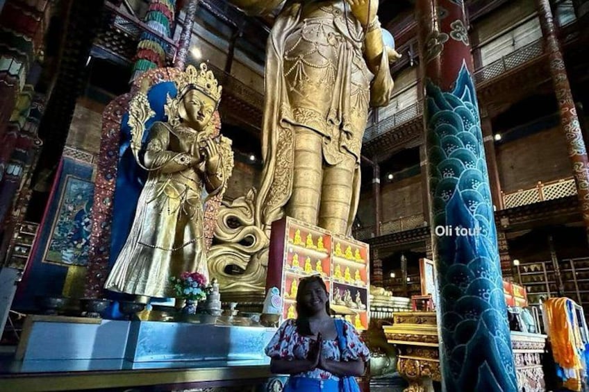 En stor gylden statue i et tempel med detaljerede udskæringer, og en kvinde bedende foran. 3