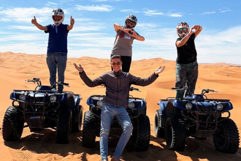 Vier personen op quad bikes in een woestijn, met zandduinen op de achtergrond. 3