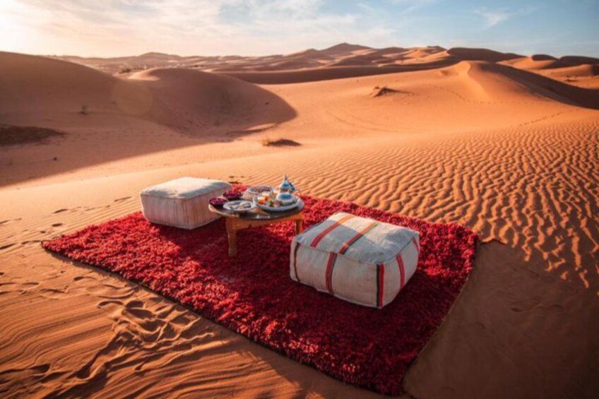 Een picknick in de woestijn met een rood kleed, een tafel met eten en twee grote kussens. 2