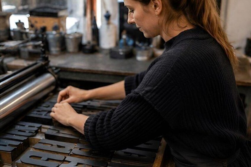 A person operating a large printing press with multiple metal plates. 4