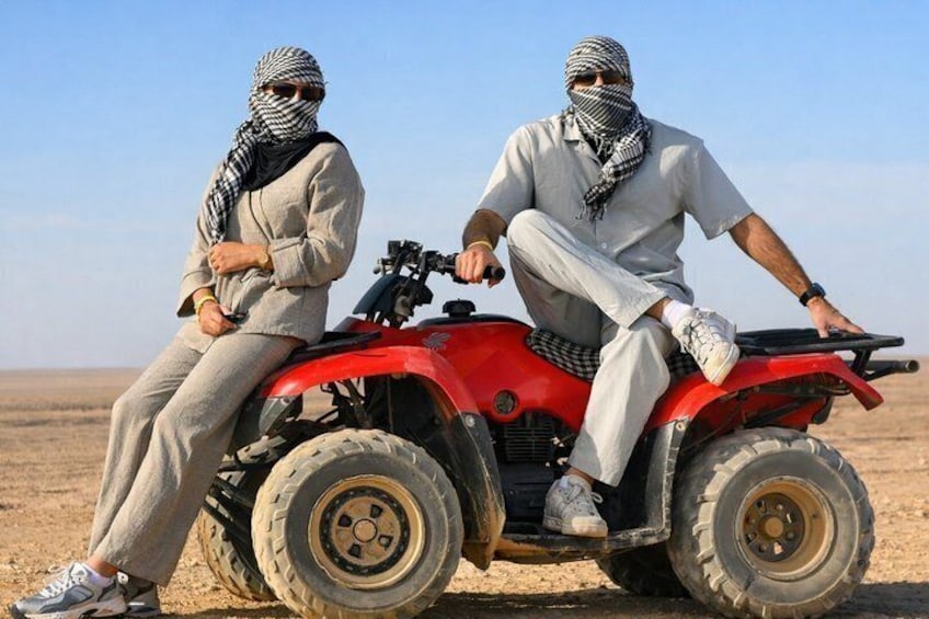 Two people sitting on a red ATV in a barren landscape. 1