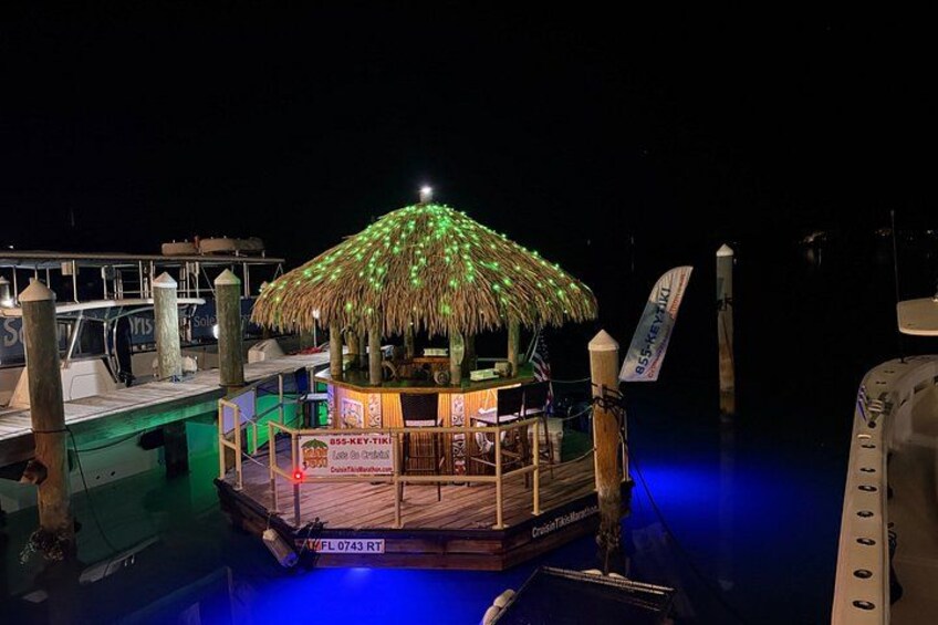 A thatched-roof structure with a sign, illuminated by blue lighting, on a dock. 4