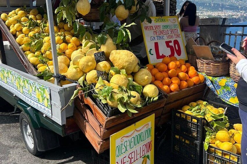 Un banco di frutta con limoni e arance, un cartello che indica un prezzo di L.50 e un'insegna con scritto 'Non toccare'. 3