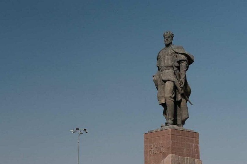 Eine Statue einer historischen Persönlichkeit auf einem Sockel mit der Inschrift 'ALEXANDER DER GROSSE' vor blauem Himmel. 2