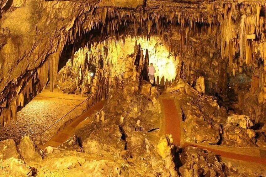 Una grotta con stalattiti, un sentiero e una persona in lontananza. 2
