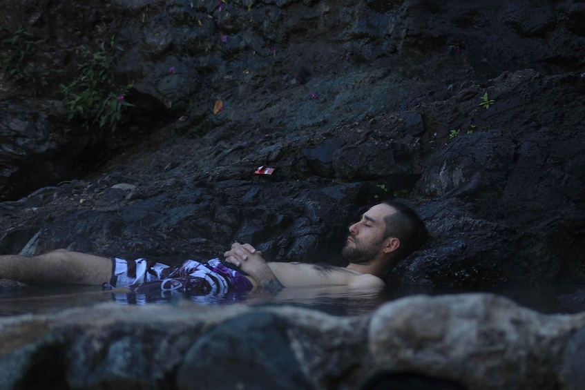 A person relaxing in a natural hot spring surrounded by rocks and vegetation. 4
