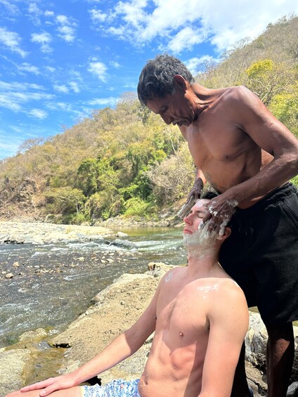 A person sitting by a river with another person washing their face. 2
