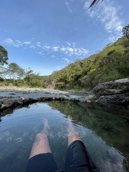 A person relaxing in a clear water body surrounded by greenery and rocks. 5