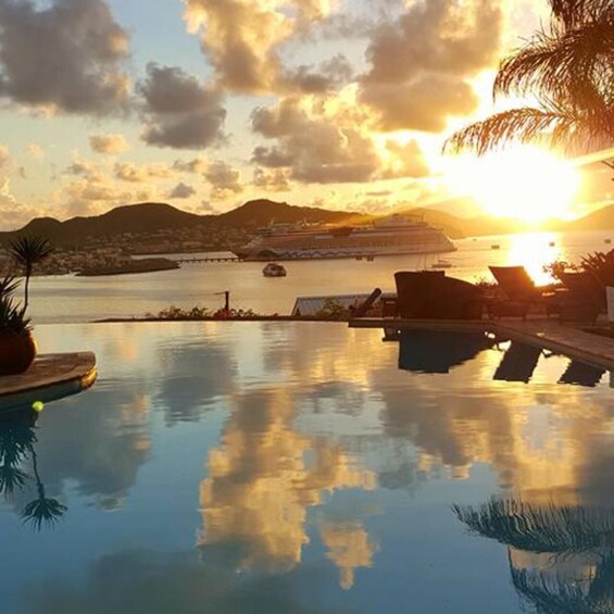 A sunset over a calm body of water with a cruise ship in the distance and lounge chairs by the pool. 5