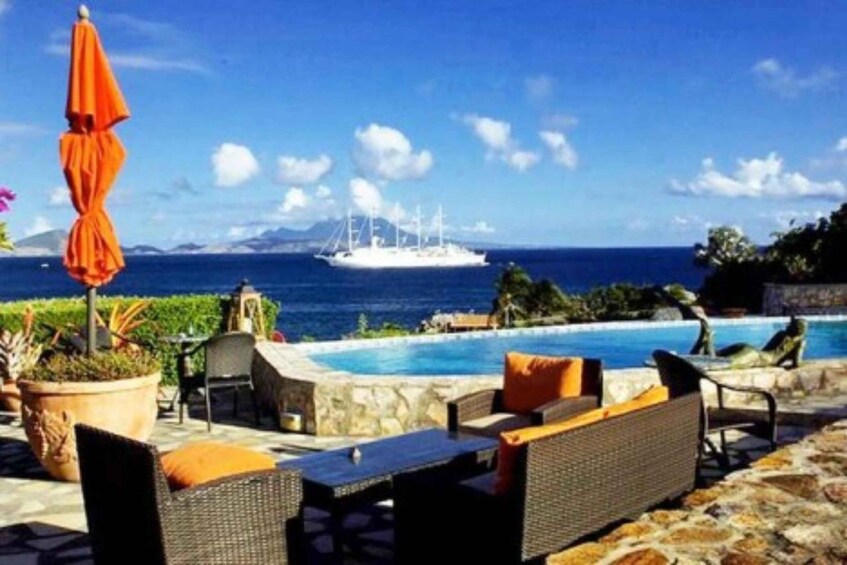 A poolside area with wicker furniture, an orange umbrella, and a view of the ocean with a ship in the distance. 4