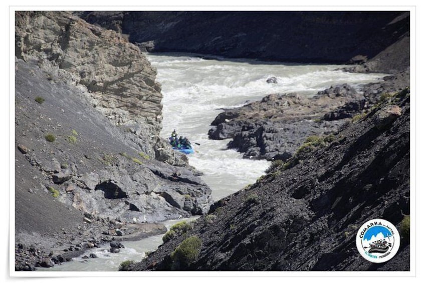Un cañón fluvial rocoso con un arroyo de aguas bravas y una balsa azul. 2