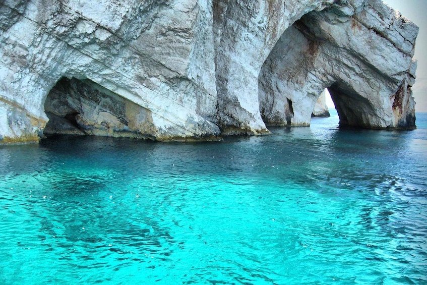 A large rock formation with a natural arch over turquoise water. 4