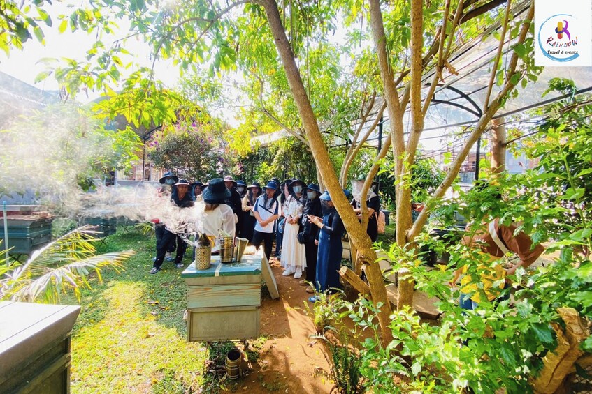 A group of people gathered around a table with a smoking device, possibly for a ceremonial purpose, in a lush outdoor setting with trees and greenery. 5