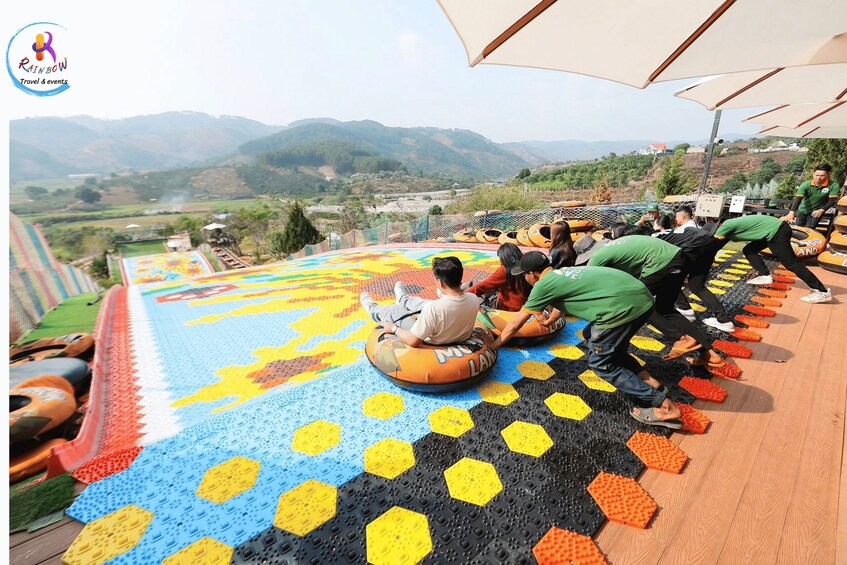 People riding colorful inflatable tubes on a mat with a scenic mountain view in the background. 2
