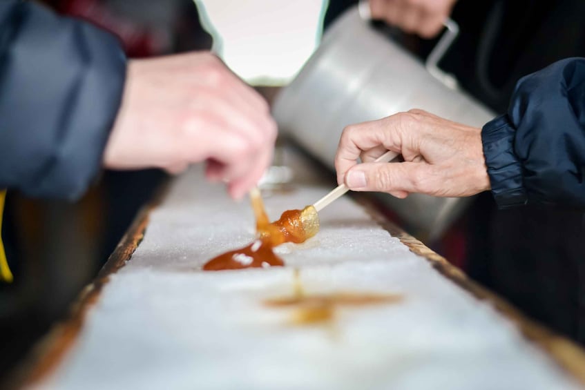 A person holding a skewer with a food item, possibly a dessert, being dipped into a sauce. 1