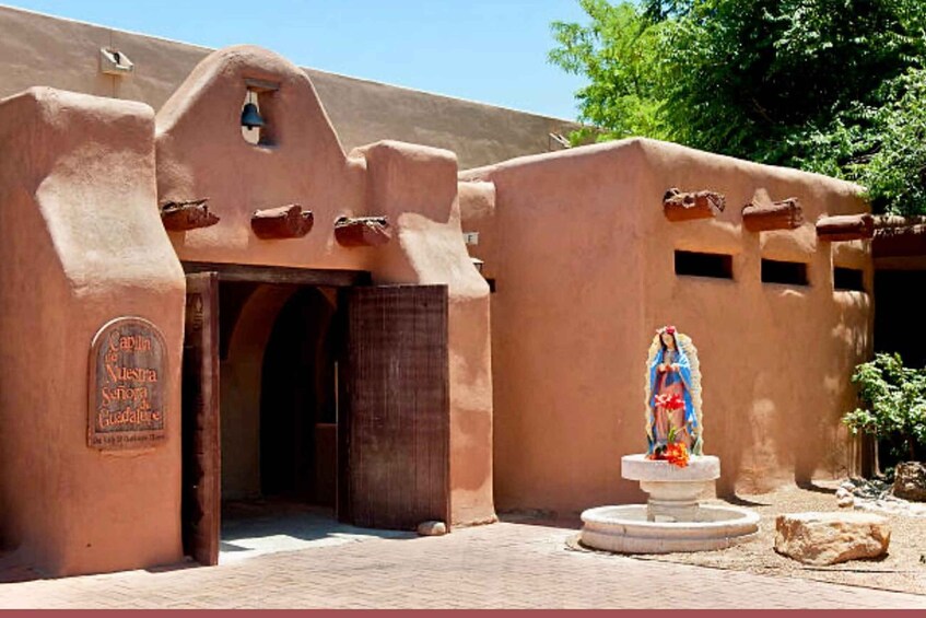 A traditional adobe building with a bell tower, a statue of the Virgin Mary, and a sign reading "Capilla de Nuestra Senora Guadalupe." 4