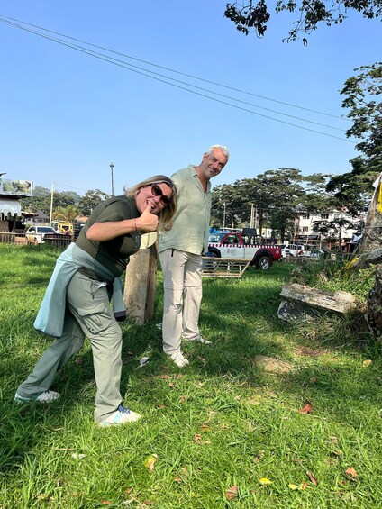 Two people standing on grass with a street and vehicles in the background. 3