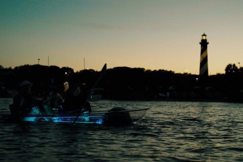 Een boot met mensen op het water bij zonsondergang, met een vuurtoren op de achtergrond. 5