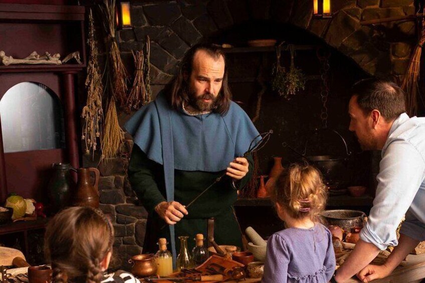 Una cocina medieval con un hombre sosteniendo una cuchara grande, una mujer con un vestido azul y un niño. 1