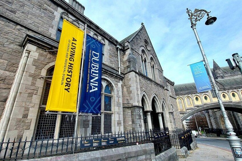 A historic building with stone architecture, banners, and a metal fence. 2