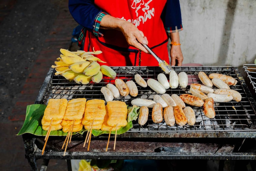 A street food vendor grilling various foods on a portable grill. 5
