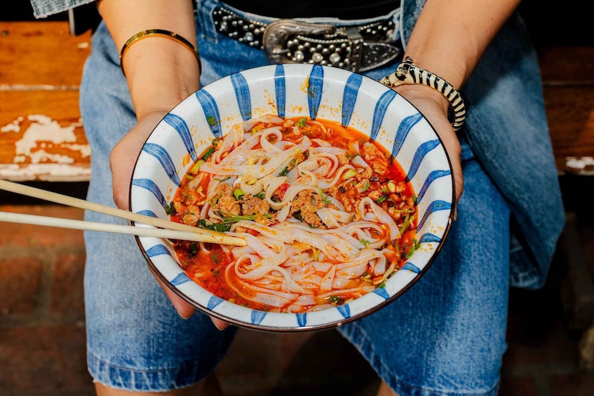 A person holding a bowl of noodle soup with chopsticks. 1