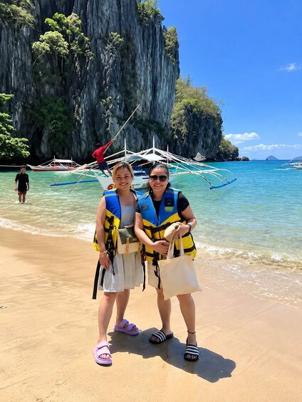 Two people on a beach with a boat and a rocky cliff in the background. 3