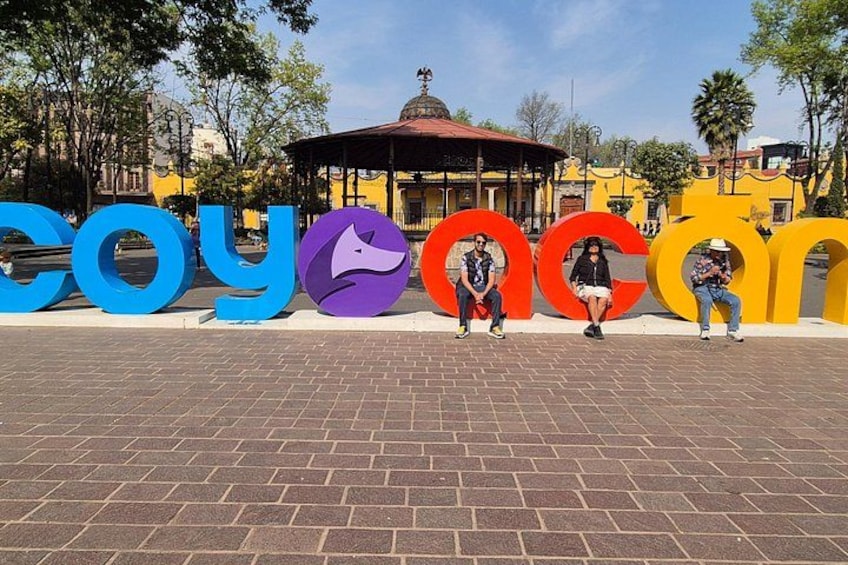 A plaza with colorful letters spelling 'cooyac' and a gazebo in the background. 3