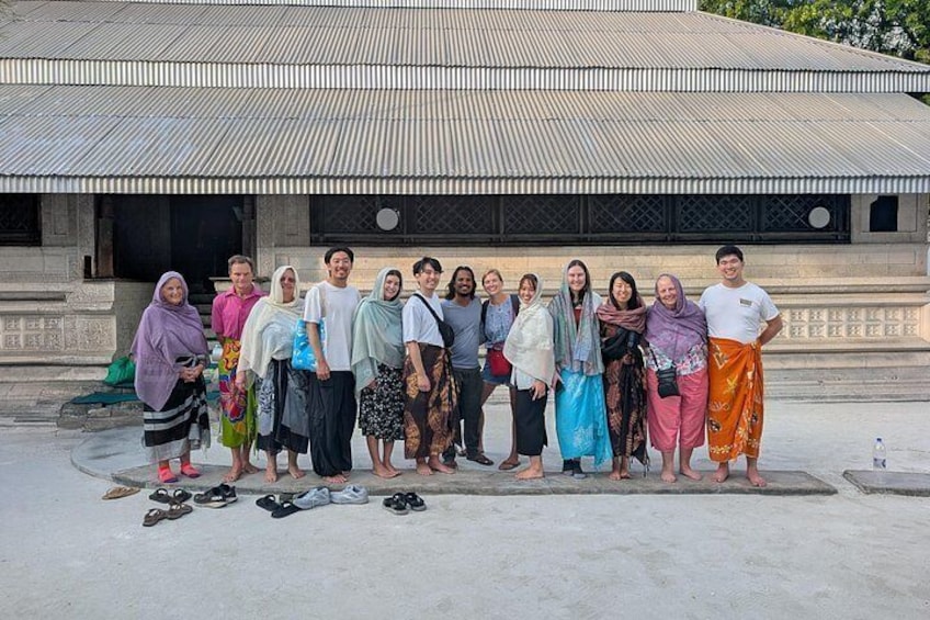 A group of people standing in front of a building with a corrugated metal roof. 1