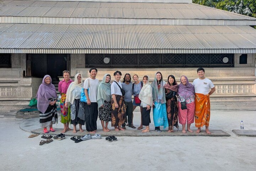 A group of people standing in front of a building with a corrugated metal roof. 1