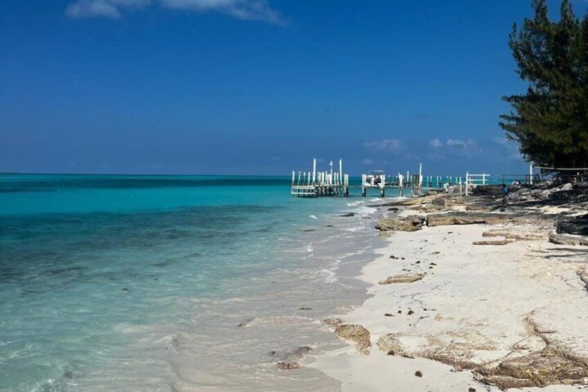A beach with clear turquoise water, white sand, and a pier with white railings. 5