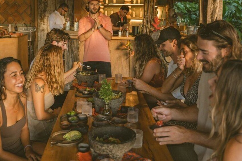 Un groupe de personnes est assis autour d’une table en bois, et déguste différents plats et boissons. 2