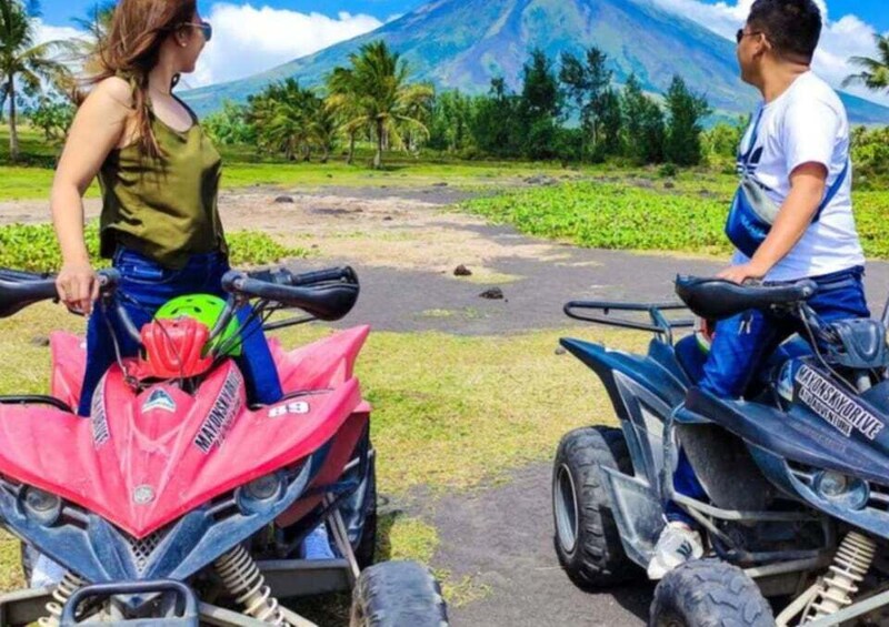 Two people on ATVs in a tropical landscape with a volcano in the background. 2