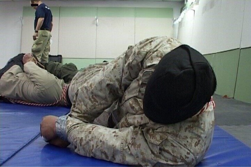 A person in military uniform lying on a mat with another person standing nearby. 2