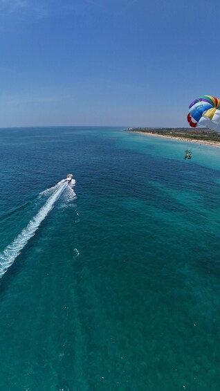 A parasail over turquoise waters with a boat creating a wake, and a beach in the distance. 2